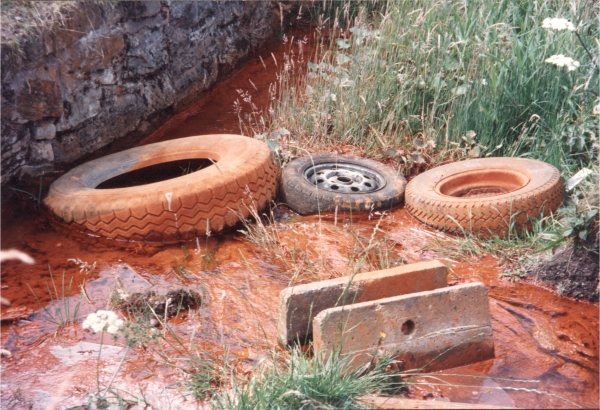Showing a stream polluted by water from old coal and iron stone mines and fly tipping next to the route followed by the North Staffordshire Railway's 'loop line' at Birchenwood nr. Kidsgrove (1994).